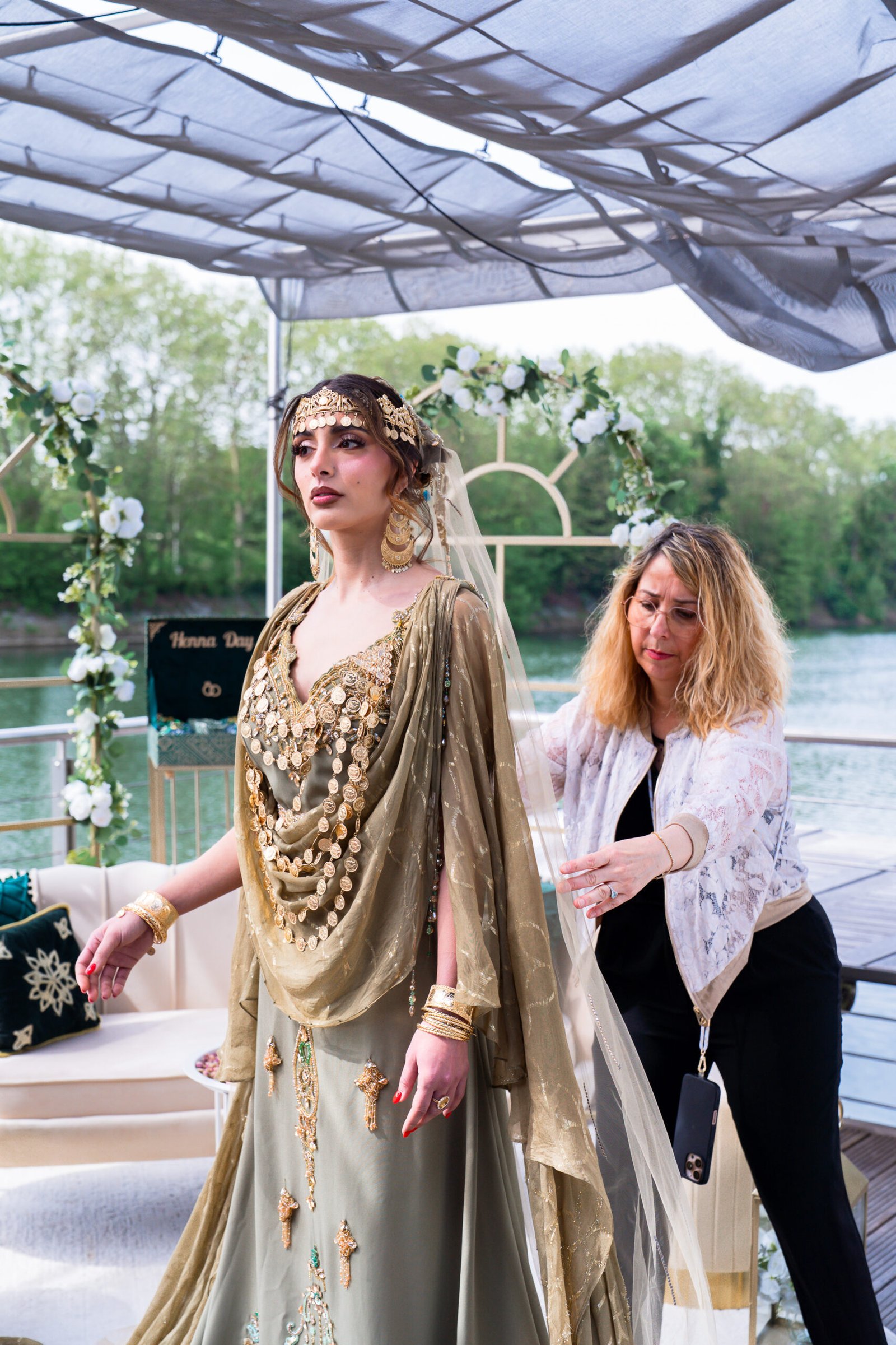 Wedding planner ajustant le voile d'une mariée en tenue traditionnelle dorée lors d'un henna day